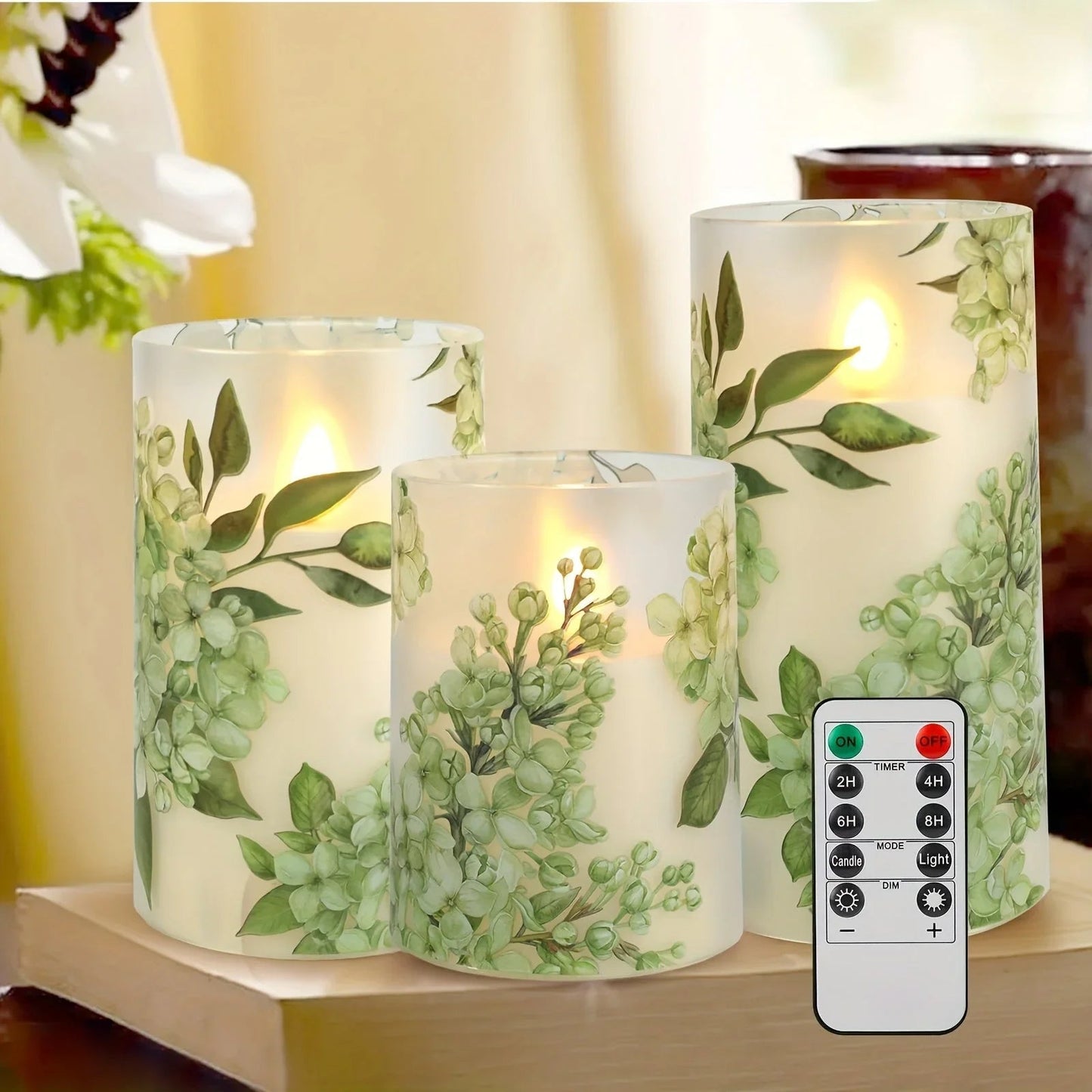 A set of 3 flameless candles, flickering LED pillar candles, with a 10-button remote control. They feature a green floral theme, are suitable for spring and summer, and can be used on the dining tables at wedding venues